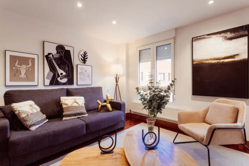 Sala de estar moderna en el apartamento Five Senses, Burgos con sofá púrpura, butaca beige, mesa de madera y vistas a la ciudad