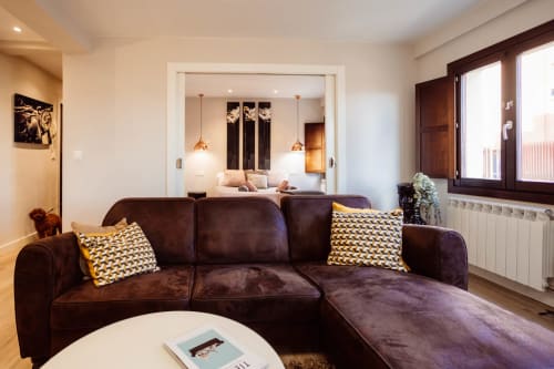 Sala moderna con sofá seccional marrón, cojines dorados, mesa de café blanca y vista al dormitorio en Arco San Esteban