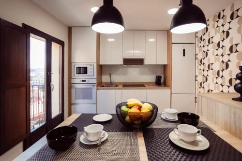 Moderna zona de cocina-comedor en apartamento Arco San Esteban, Burgos, con lámparas colgantes negras y papel tapiz geométrico