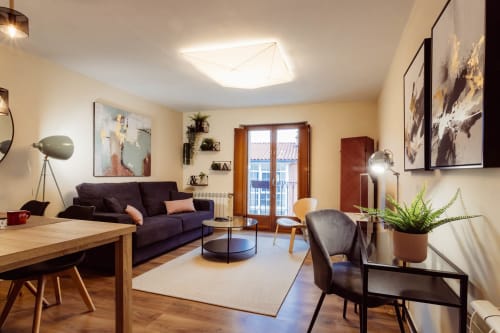 Moderna sala de estar en Burgos con sofá oscuro, mesa de comedor de madera, plantas y puertas de balcón con vistas a la ciudad
