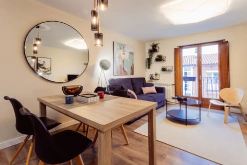Moderno apartamento en Burgos con mesa de comedor de madera, sofá púrpura, espejo redondo y balcón con vistas a la ciudad en Unique