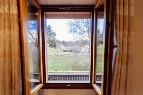 Puertas de madera abiertas con vistas de la ciudad, colinas verdes ondulantes y árboles de bosque desde el apartamento The Charm en Burgos, España