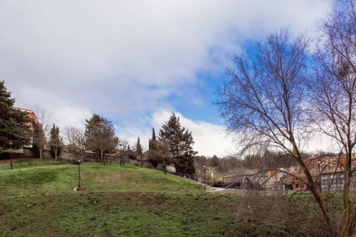 Parque de ladera verde en Burgos con árboles desnudos, edificios de la ciudad y cielo azul - vista desde el apartamento Unique Rooms