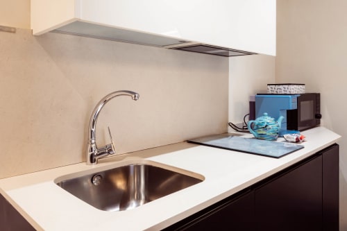 Moderna cocina con fregadero de acero inoxidable, grifo cromado, encimera blanca y salpicadero beige en apartamento de Burgos