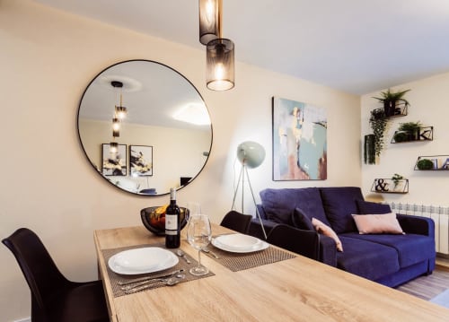 Comedor moderno de apartamento con mesa de madera, sofá púrpura, espejo redondo y vistas a la ciudad en hotel de Burgos