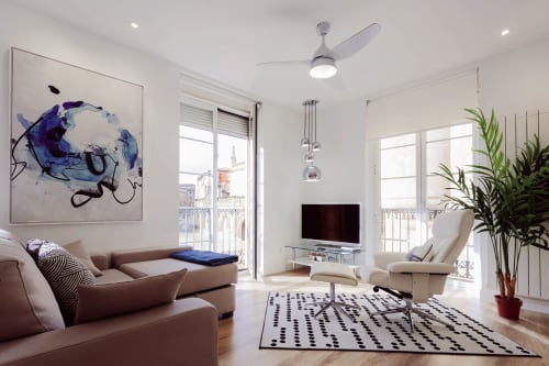 Elegante sala de estar en apartamento de Burgos con sofá beige, arte abstracto, vista de la catedral desde balcón, ventilador de techo y plantas