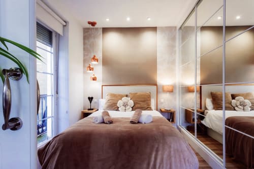 Dormitorio moderno con ropa de cama marrón, armario espejo, luces colgantes y balcón con vistas a la Catedral de Burgos
