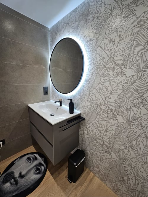 Baño moderno en apartamento de Burgos con espejo ovalado iluminado, lavamanos blanco y diseño de papel tapiz con motivos botánicos