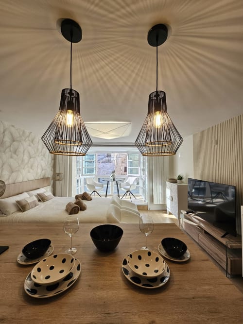 Moderno apartamento en Burgos con lámparas colgantes, zona de comedor, cama y vistas a la catedral desde las puertas del balcón