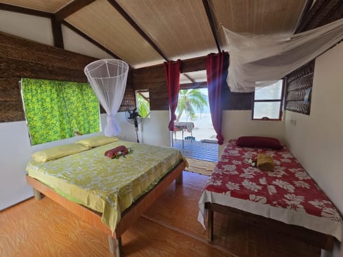 Fare Tauhei bedroom at Tikehau Herearii with two beds, mosquito nets, and sea view terrace in Tuherahera