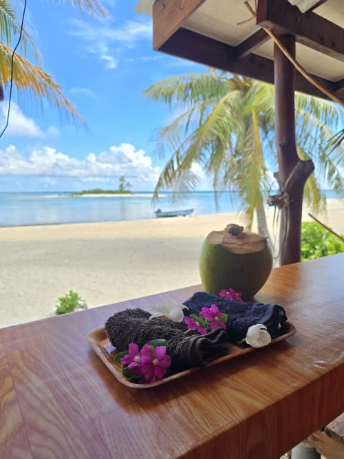 Tropical beach setting at Tikehau Herearii with coconut drink, spa treatment platter, and ocean view from overwater bungalow