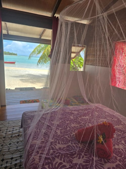 Beachfront bedroom with mosquito net canopy at Tikehau Herearii, PF, overlooking turquoise lagoon and palm trees