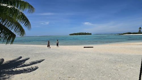 Pristine turquoise lagoon beach at Tikehau with palm shadows, white sand, and two people wading in crystal clear water