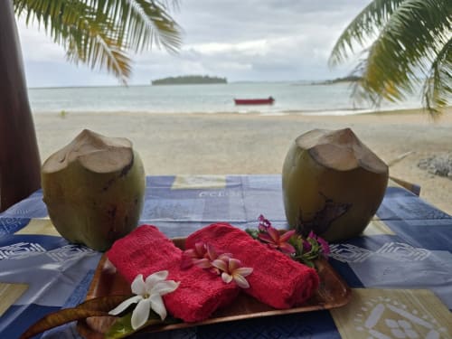 Two fresh coconuts and tropical flowers on red towel with ocean view at Tikehau Herearii beachfront room in French Polynesia