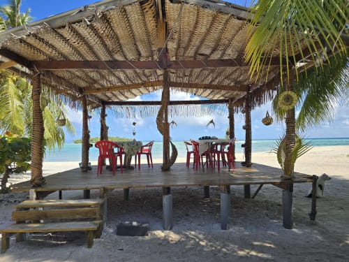 Thatched beachside bungalow with red chairs at Tikehau Herearii in French Polynesia, featuring ocean views and palm trees