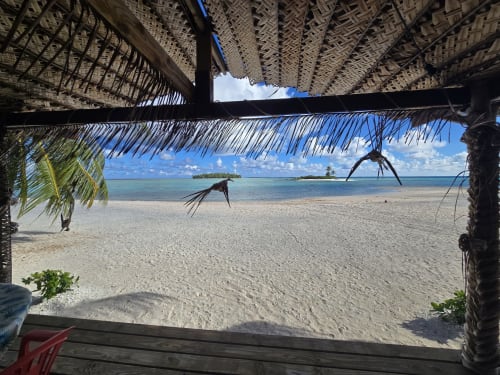 Tikehau Herearii beachfront bungalow view with white sand, turquoise lagoon, and palm thatch roof in Tuherahera