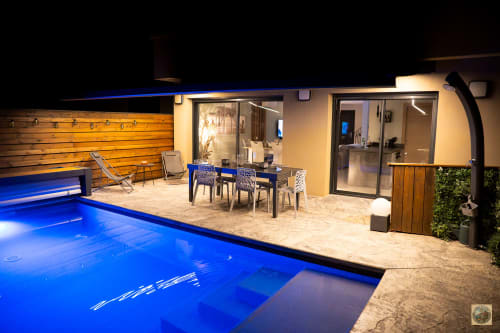 Nighttime view of Villa Core di Favona pool with illuminated blue water, patio dining area, and modern home in Favone, managed by Corsu di Core conciergerie