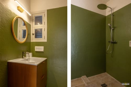 Salle de bain moderne avec carrelage vert, meuble-lavabo en bois, miroir rond et douche à l'italienne à La Conciergerie du Cap Corse