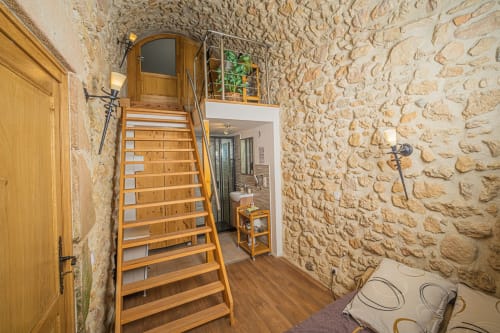 Escalier en bois dans la chambre troglodyte du Château de Villelongue, aux murs rustiques et porte en bois