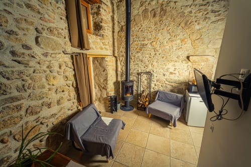 Suite principale l'étable au Château De Villelongue avec murs en pierre, lits, TV, ventilateur et coin salon à Villelongue-d'Aude