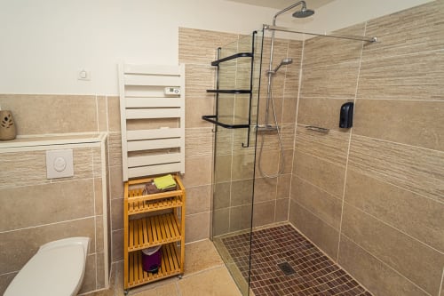 Salle de bain moderne avec douche ouverte, sèche-serviettes chauffant et rangements en bois à l'Au Château De Villelongue B&B
