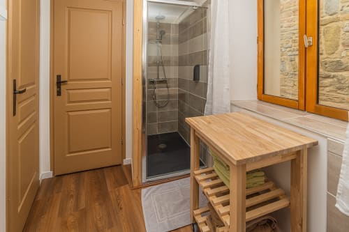 Salle de bain moderne avec douche à l'italienne, meuble-lavabo en bois et détails en pierre au gîte Au Château De Villelongue