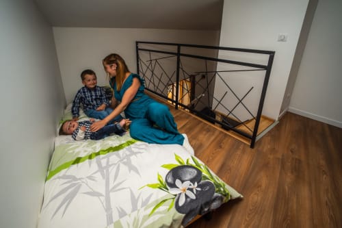 Femme et deux enfants détendus sur un lit avec linge de lit à thème nature dans la chambre School du Château De Villelongue,