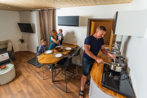 Famille dans la cuisine-salle à manger moderne du Château de Villelongue, l'homme cuisine tandis que les enfants sont à table
