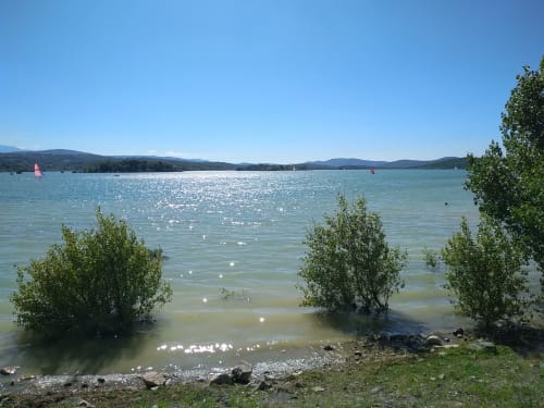 Lago turquesa con veleros, árboles verdes y montañas al fondo cerca de Villelongue-d'Aude