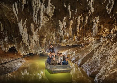 Visitantes en un tour en bote subterráneo a través de una caverna de piedra caliza iluminada cerca de Villelongue-d'Aude, Francia
