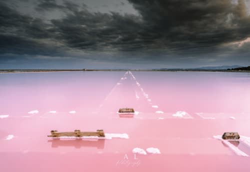 Lago de sal rosa surrealista con estructuras de madera y cielo oscuro, cerca del Château de Villelongue en Villelongue-d'Aude, Francia