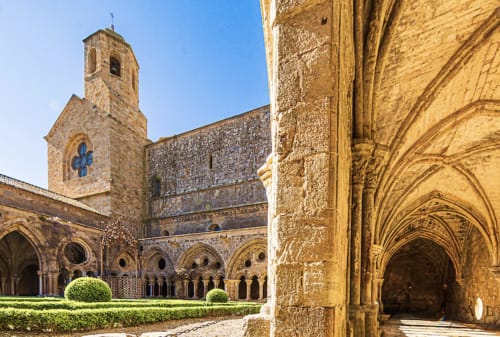 Claustros medievales del Château de Villelongue con columnas arqueadas, jardines cuidados y campanario en Villelongue-d'Aude