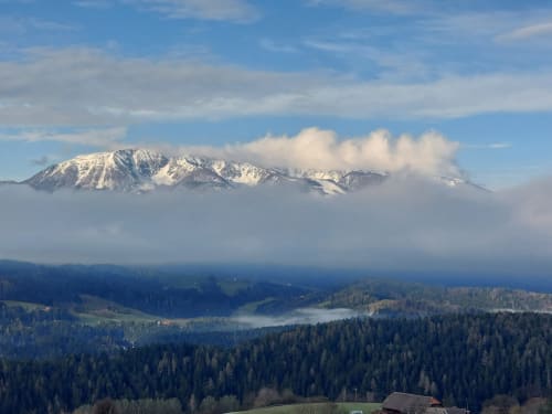 Snow-capped mountain peak above forested valleys near Kmetija Pečnik in Prevalje, Slovenia