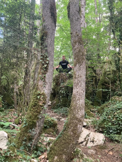 Hombre meditando en un sendero forestal entre árboles cubiertos de musgo en el Château De Villelongue