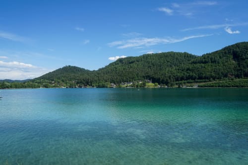Turquoise alpine lake with forested mountains and lakeside village near Prevalje, Slovenia
