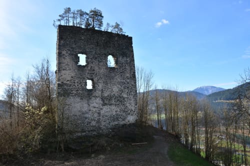 Ruined stone tower surrounded by bare trees and mountains in Prevalje, Slovenia