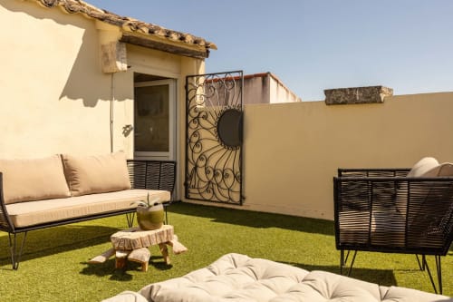 Sunny rooftop terrace at Le Prieuré Notre-Dame in Montfrin with lounge seating, artificial grass, and decorative iron gate.