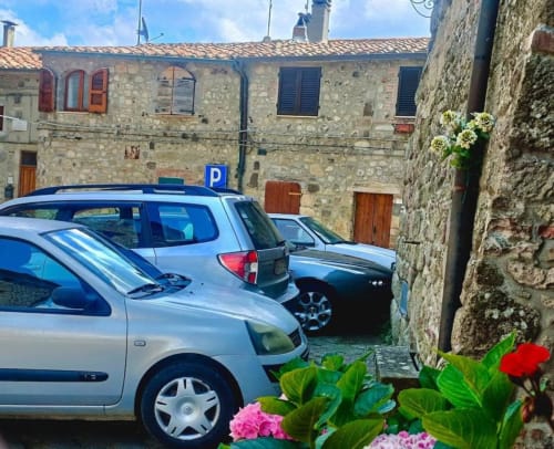 Parcheggio della Torre Della Chiocciola B&B a Monteriggioni con edifici medievali in pietra e fiori colorati