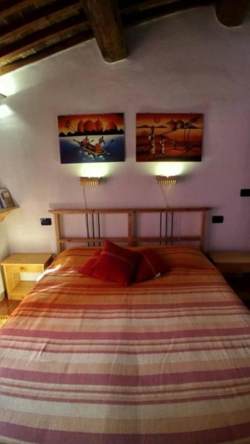 Camera da letto Torre Della Chiocciola Monteriggioni con letto in legno, biancheria a righe, quadri illuminati e travi a vista