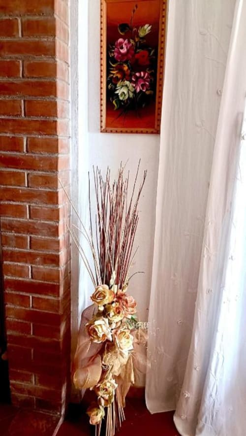 Stretto corridoio con muro in laterizio, composizione floreale decorativa con graminacee secche e dipinto di fiori incorniciato in appartamento B&B