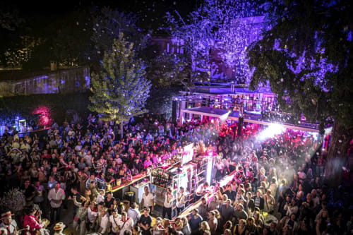Vibrant nighttime outdoor event at Le Prieuré Notre-Dame in Montfrin with colorful purple and pink lighting, large crowd, and