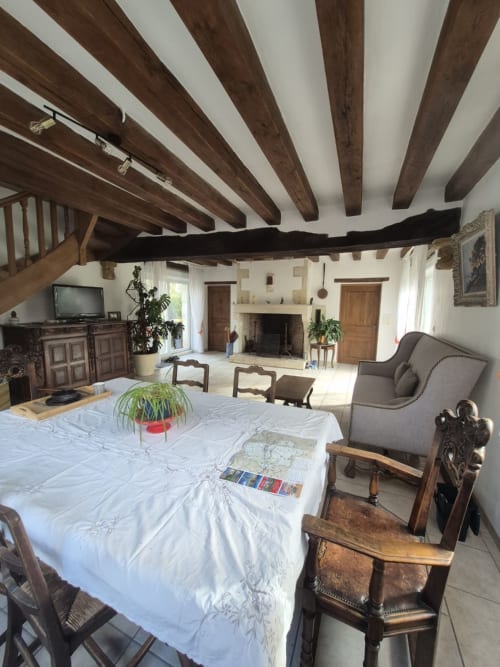 Spacieuse salle à manger avec poutres en bois apparent au gîte Le Moulin Garnier, nappes blanches et mobilier rustique