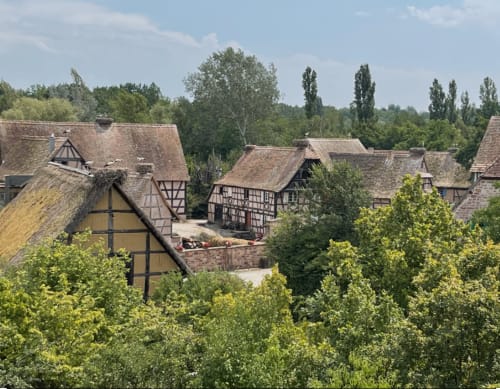 Maisons à colombages médiévales aux toits de chaume à Cernay, France, nichées parmi des arbres verdoyants sous un ciel bleu