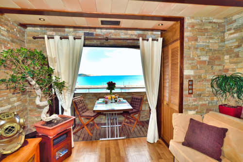 Suite balcon luxe au B&B Banyuls avec vue mer, table à manger, rideaux crème et murs en pierre donnant sur la Méditerranée.