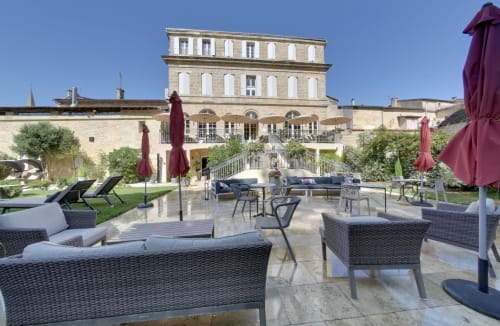 Elegant courtyard at Pavillon Des Millesimes in Lussac with wicker seating, burgundy umbrellas, and manicured gardens