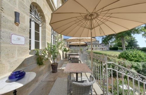 Elegant terrace at Pavillon Des Millesimes in Lussac with beige umbrellas, dining tables, and manicured grounds view.