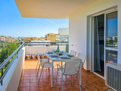 Soleada terraza del apartamento SACORO Marbella con mesa de comedor con vistas a edificios amarillos y jardines