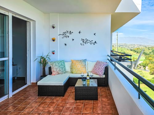 Balcón moderno con zona de descanso, cojines coloridos y vistas panorámicas del jardín en el hotel SACORO, Marbella
