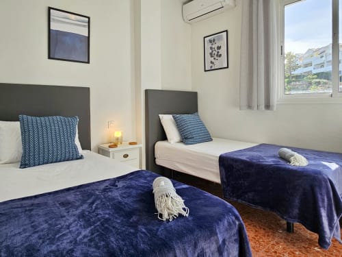 Dormitorio doble con colchas de terciopelo azul oscuro en apartamento SACORO en Marbella, vista al jardín