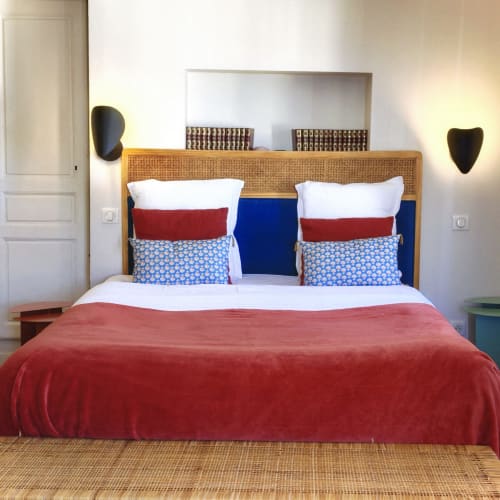 Chambres Sancy à La Tour Grégoire : chambre moderne avec tête de lit en rotin, couette rouge, touches bleues et murs neutres